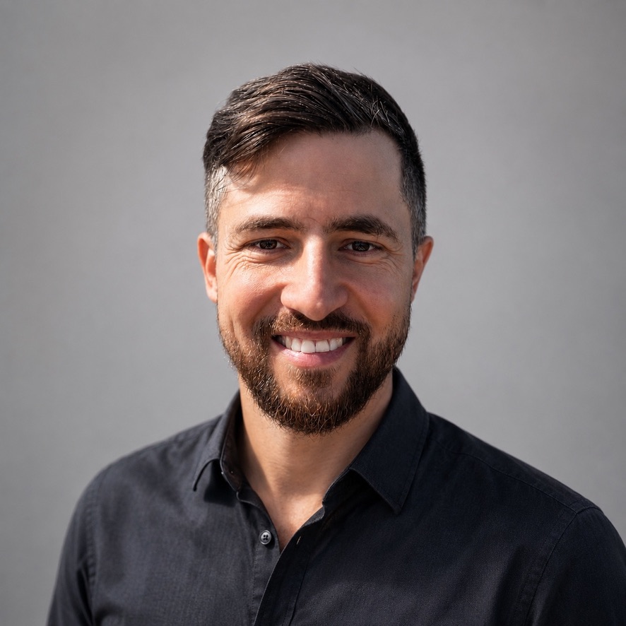 Mike Majewski, smiling, wearing a dark button-up shirt against a plain grey background